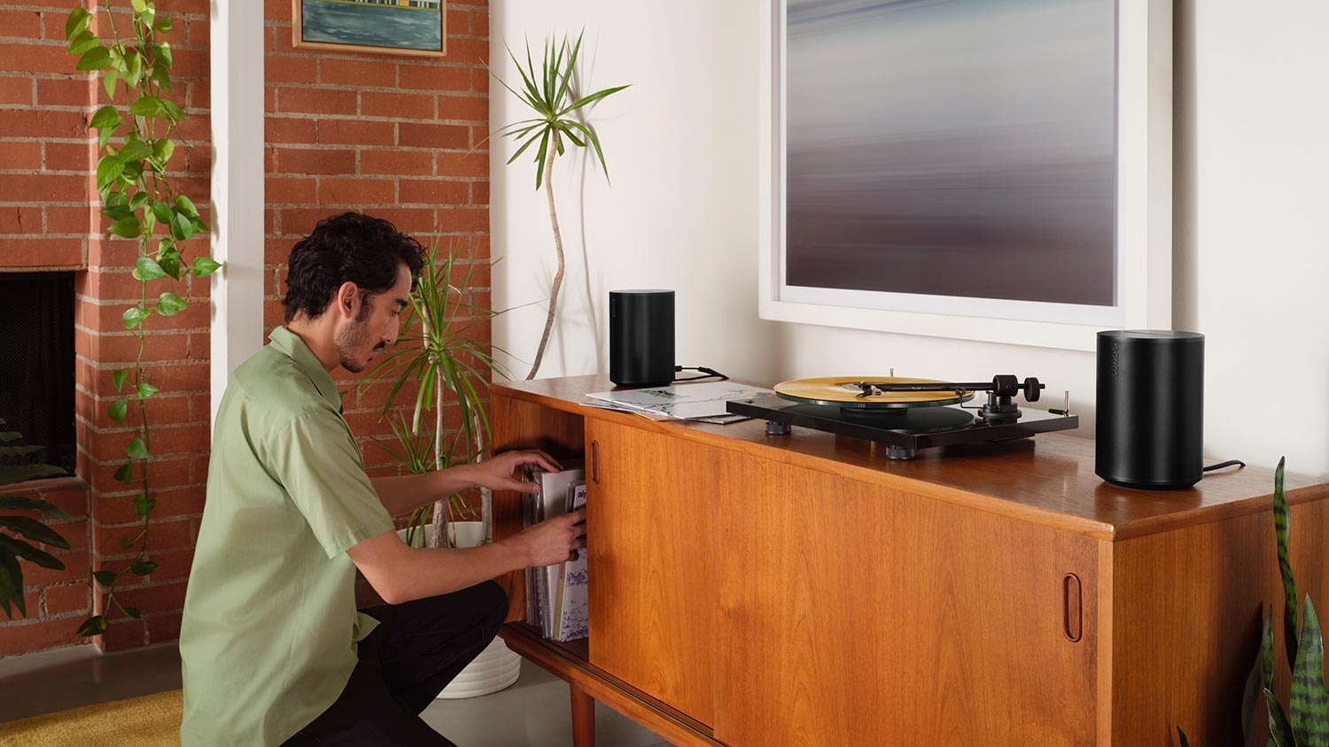 Man playing records in a turntable with Sonos Era 100 speakers in black